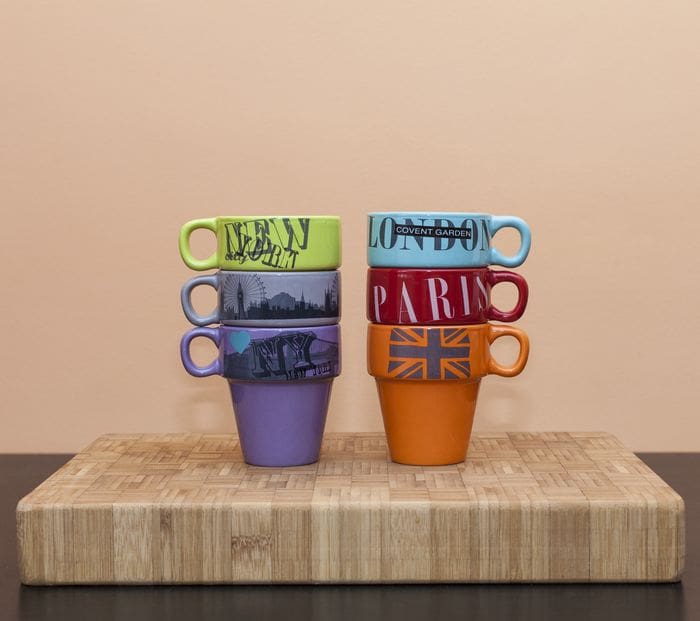 two stacks of colored coffee mugs with the names of different cities on them